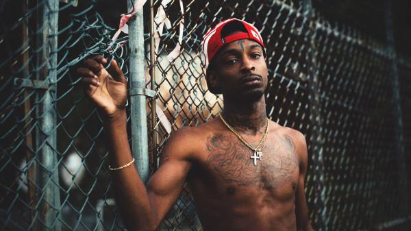 Free 21 savage is wearing chains on neck and red cap having tattoos standing in front of chain link fence hd 21 savage wallpaper download