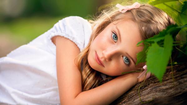 Free ash eyes cute little girl is lying on tree trunk wearing white dress in green background hd cute wallpaper download