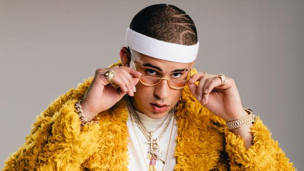 Free bad bunny aesthetic is wearing yellow dress in ash background wearing gold chains holding specs with hands hd music wallpaper download