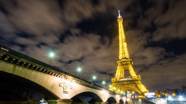 Free bridge side view of yellow lighting paris eiffel tower with background of dark sky and clouds hd travel wallpaper download