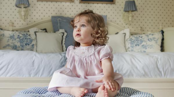 Free cute ash eyes baby girl is sitting on bed wearing pink dress hd cute wallpaper download