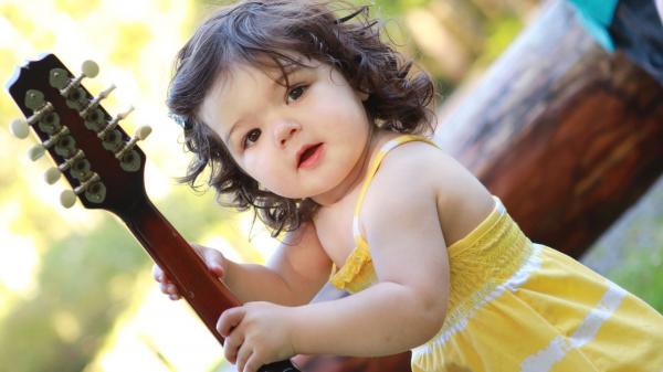 Free cute baby girl is having guitar in hand wearing yellow dress standing in a blur background hd cute wallpaper download