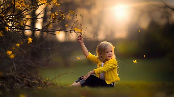 Free cute baby girl is sitting on green grass touching flower wearing yellow dress with sunlight background hd cute wallpaper download