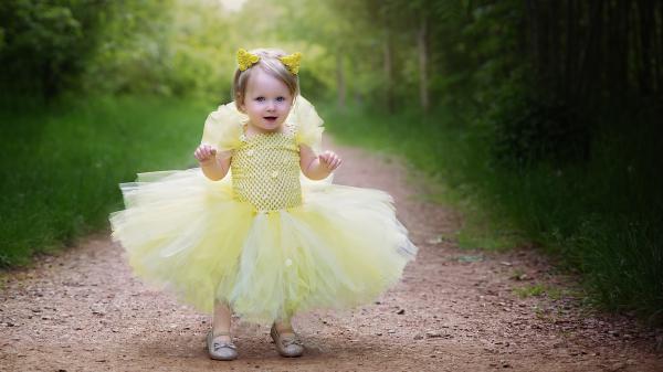 Free cute baby girl is wearing yellow dress standing on road in green trees background hd cute wallpaper download