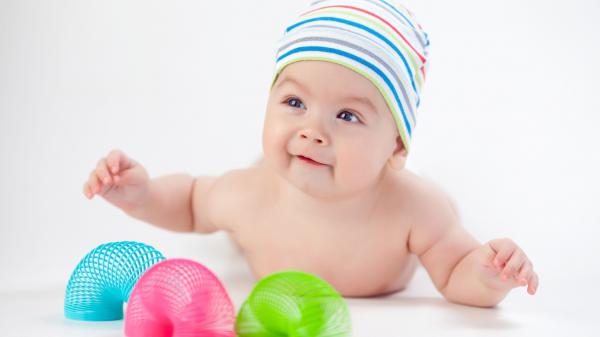 Free cute baby is lying down on floor playing with toys wearing cap in a white background hd cute wallpaper download