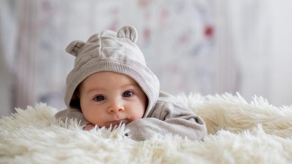 Free cute baby is lying down on sandal woolen bed wearing bunny cap 4k hd cute wallpaper download