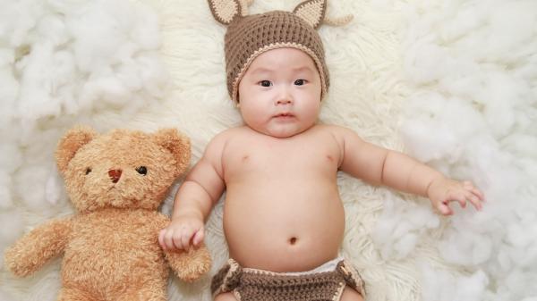 Free cute baby is lying on white cushion beside brown bear toy hd cute wallpaper download