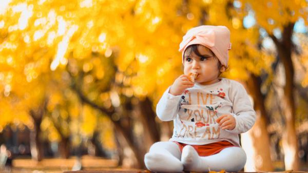 Free cute baby is sitting on top of table wearing white dress in a yellow blur background hd cute wallpaper download