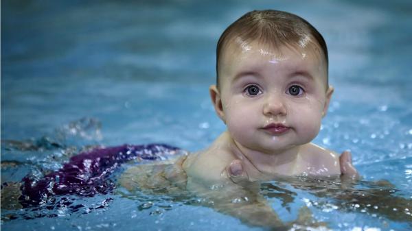 Free cute baby is swimming on body of water wearing purple shorts in a blur water background hd cute wallpaper download