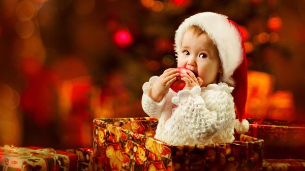 Free cute girl baby inside gift box wearing santa cap and sandal color dress biting apple in blur light background 4k hd cute wallpaper download