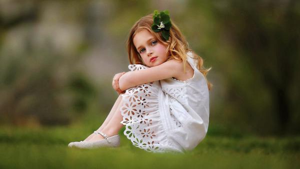 Free cute girl baby is wearing white dress sitting on grass facing one side and having green leaves on head in a blur background hd cute wallpaper download