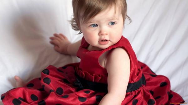 Free cute girl baby with ash eyes is sitting on white bed wearing red dress hd cute wallpaper download