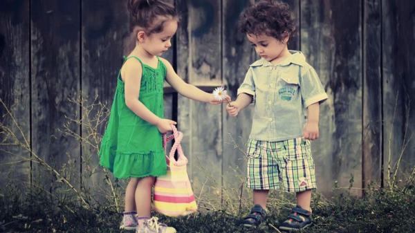 Free cute little girl is giving flower to the boy wearing green and ash dress in wooden background hd cute wallpaper download