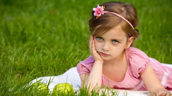 Free cute little girl is holding face with one hand lying down on grass wearing pink white dress hd cute wallpaper download