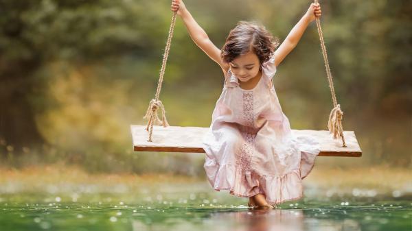 Free cute little girl is wearing light peach dress riding on swing over river during daytime 4k hd cute wallpaper download