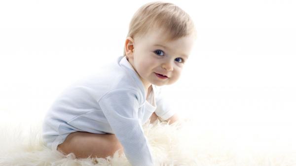 Free cute smiley baby boy is sitting down on white woolen floor carpet posing for a photo wearing white dress hd cute wallpaper download