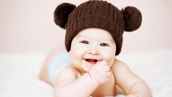 Free cute smiley baby is wearing brown knitted woolen cap having hand on mouth hd cute wallpaper download