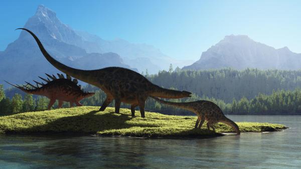 Free dinosaurs are on grass field drinking water with mountain and blue sky background hd dinosaur wallpaper download