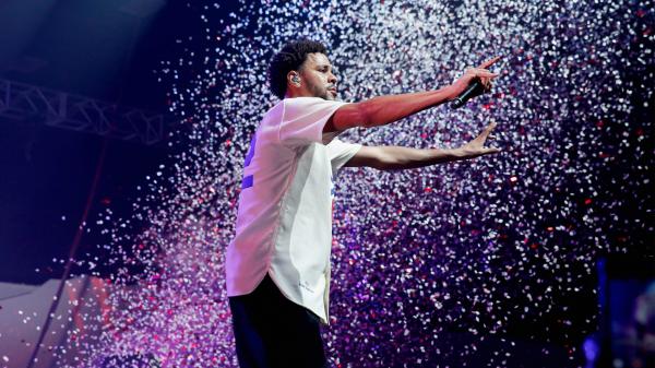 Free j cole is standing on stage wearing white shirt having mike in hand hd music wallpaper download