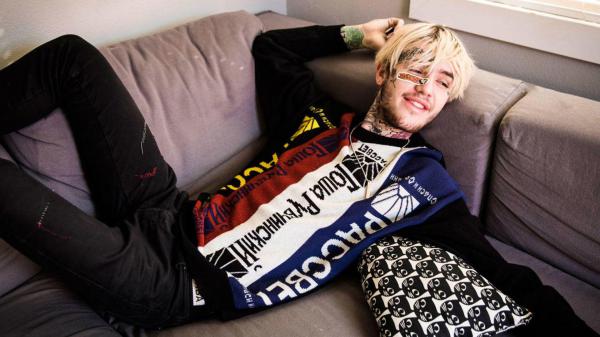 Free lil peep is lying back on couch wearing colorful tshirt having tattoos on neck and hands hd music wallpaper download