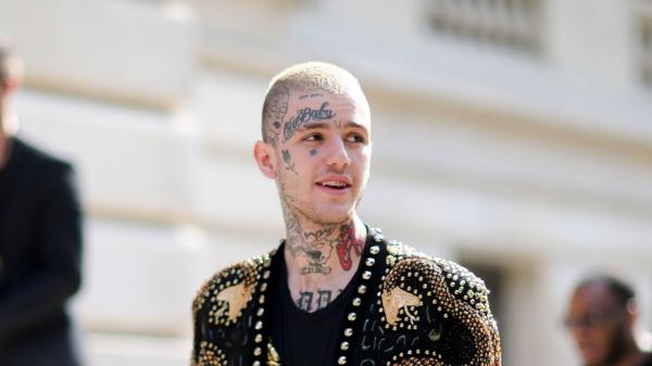 Free lil peep is standing in blur background wearing black coat and having tattoos on face and neck facing one side hd music wallpaper download