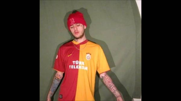 Free lil peep is wearing red and yellow tshirt and red cap standing in forest green background having tattoos on hands hd music wallpaper download