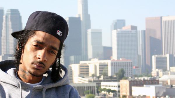 Free nipsey hussle in blur building background wearing ash coat and black cap hd music wallpaper download