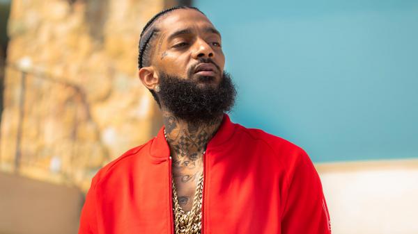 Free nipsey hussle is looking side and wearing red coat and having tattoos and chains on neck in a blur blue background 4k hd music wallpaper download