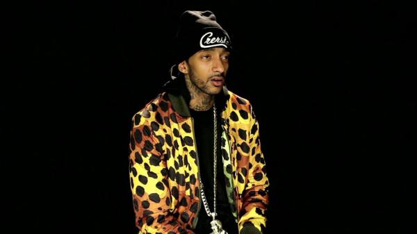 Free nipsey hussle is wearing colorful coat and black cap in a black background hd music wallpaper download