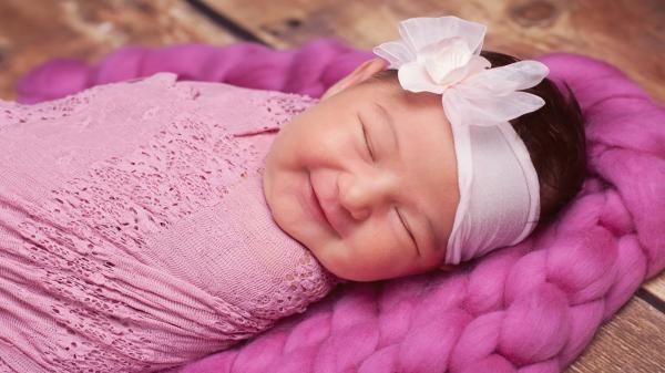 Free smiley cute closed eye baby is covered with pink netted towel and having white ribbon band on head hd cute wallpaper download