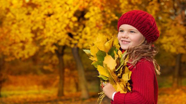 Free smiley cute girl is wearing red wool knitted sweater and cap having dry leaves in hands in autumn trees background hd cute wallpaper download