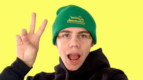 Free the kid laroi is wearing black t shirt and green woolen cap on head showing victory sign in yellow background hd the kid laroi wallpaper download