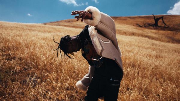 Free travis scott is looking down standing on dry grass in sky background wearing black dress and overcoat hd travis scott wallpaper download