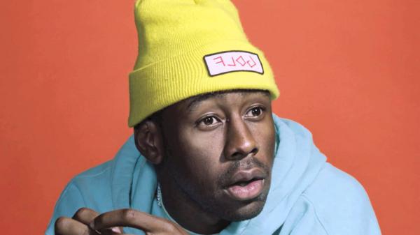 Free tyler the creator in a light orange background wearing blue cap tshirt and yellow woolen cap hd music wallpaper download