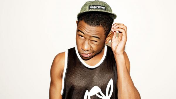 Free tyler the creator is wearing supreme green cap and black sleeveless tshirt with one eye closed in a white background hd music wallpaper download